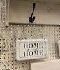 A white enamel sign with black lettering and hangs from a wire hanger. The sign says Home sweet home.