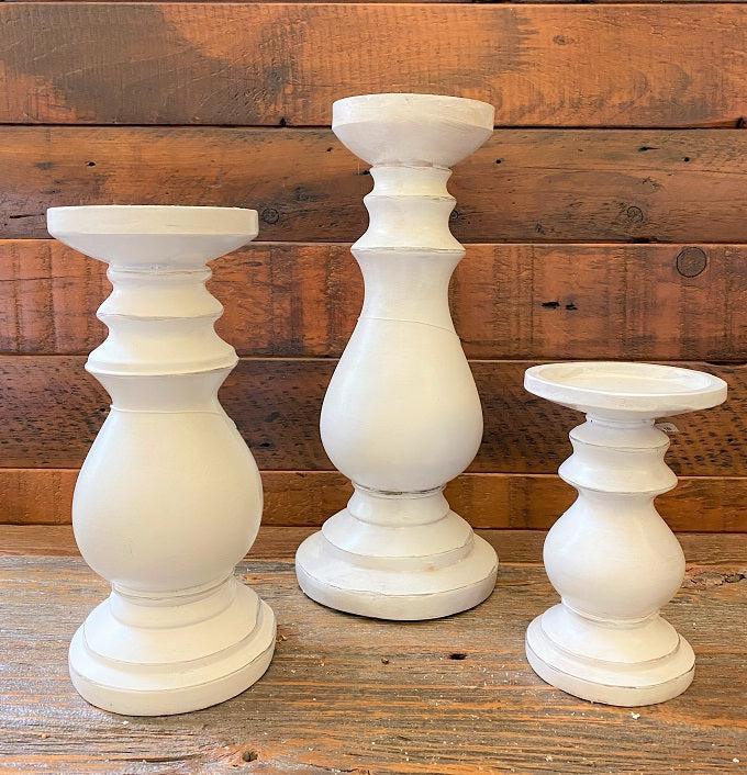 Three distressed white wooden candle holders. They are turned wood round holders and are painted white with some light distressing all over.