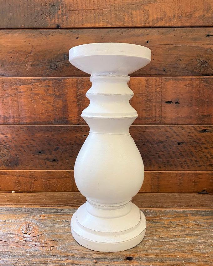 A distressed white wooden candle holder. It is a turned wood round holder and is painted white with some light distressing all over it. 