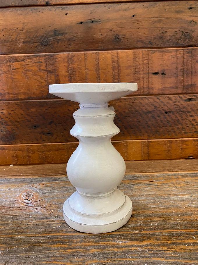 A distressed white wooden candle holder. It is a turned wood round holder and is painted white with some light distressing all over it. 