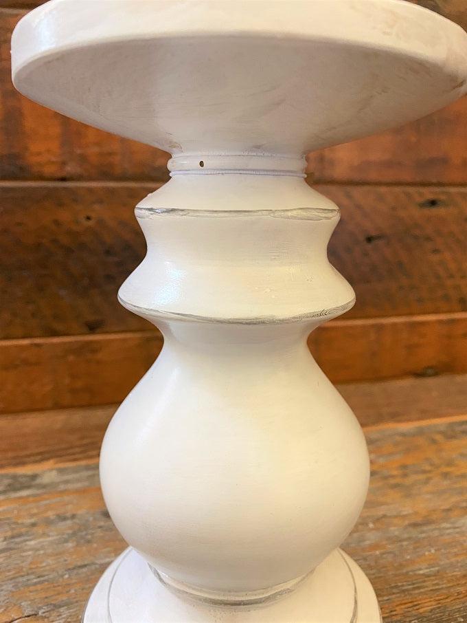 A close up of a distressed white wooden candle holder. It is a turned wood round holder and is painted white with some light distressing all over it. 