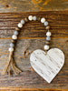 The Chippy Beaded Heart Swag is a white heart attached to a short string of brown, white and grey beads.