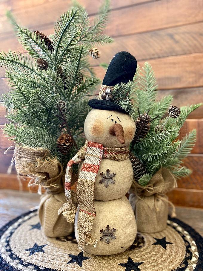 The Cranberrry plaid scarf snowman is a three stack snowman and has a black hat with cranberry and tan plaid trim and matching scarf. There  is a jingle bell trim on his hat and one metal snowlake on his middle and bottom stack. He has two twiggy arms. 