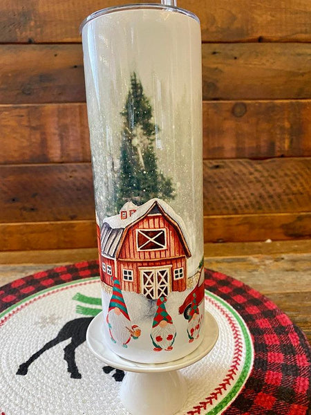 The Christmas Gnome Hot/Cold Tumbler bottle is wrapped in a pretty christmas  scene with a classic red barn and snow-filled evergreen trees. 