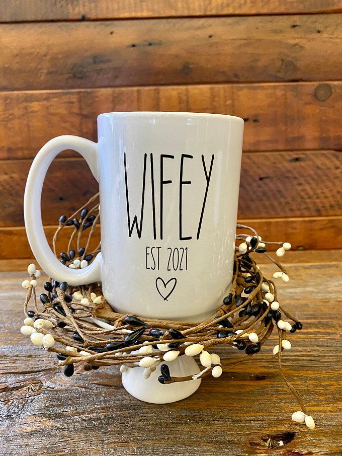 A white ceramic mug with the words WIFEY Est 2021 and a small heart is printed in black. The mug is customizable to the year.
