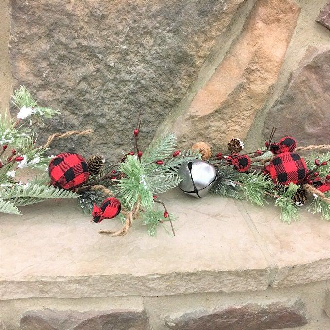 A  garland made up of snowy Christmas greens, silver jingle bells and round red and black check fabric coloured balls, pine cones and jute rope.