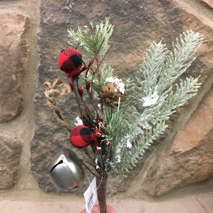 A  pick made up of snowy Christmas greens, silver jingle bells and round red and black check fabric coloured balls, pine cones and jute rope.