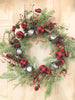 A beautiful Christmas wreath filled with snowy Christmas greens, silver jingle bells and round red and black check fabric coloured balls and pine cones and sprigs of jute rope.