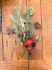 A  pick made up of snowy Christmas greens, and round red and black check fabric coloured balls, pine cones and jute rope.