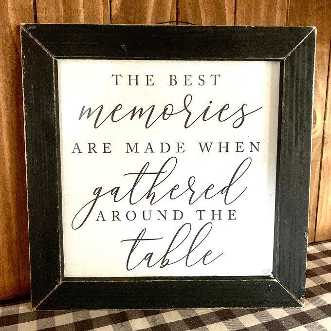 A square framed sign, with a black frame with some distressing on it. the sign is written in upper case and cursive style lettering and says: The best memories are made when gathered around the table. 