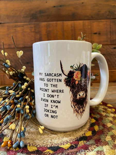 A white mug with a painted picture of a cow with long horns and flowers on its head on to the right of the following words: My sarcasm has gotten to the point where I don't even know if I'm joking or not."