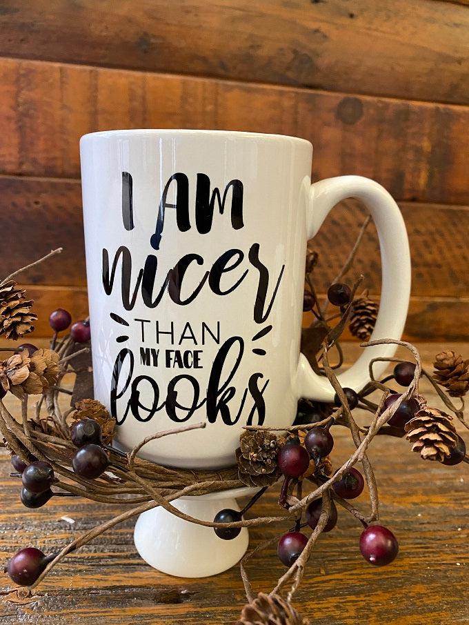 A white ceramic mug with the text I am nice than my face looks is printed in black.