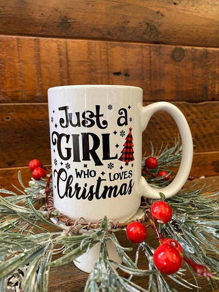 The Just a Girl who loves Christmas mug. The text is a variety of fonts and all in black. There is a red checked Christmas tree on it as well. 