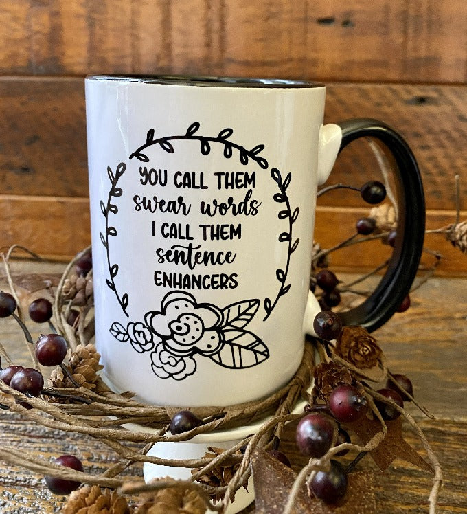 A white ceramic mug with a black handle and black inside. The mug is printed on both sides and says You call them swear words I call them sentence enhancers.